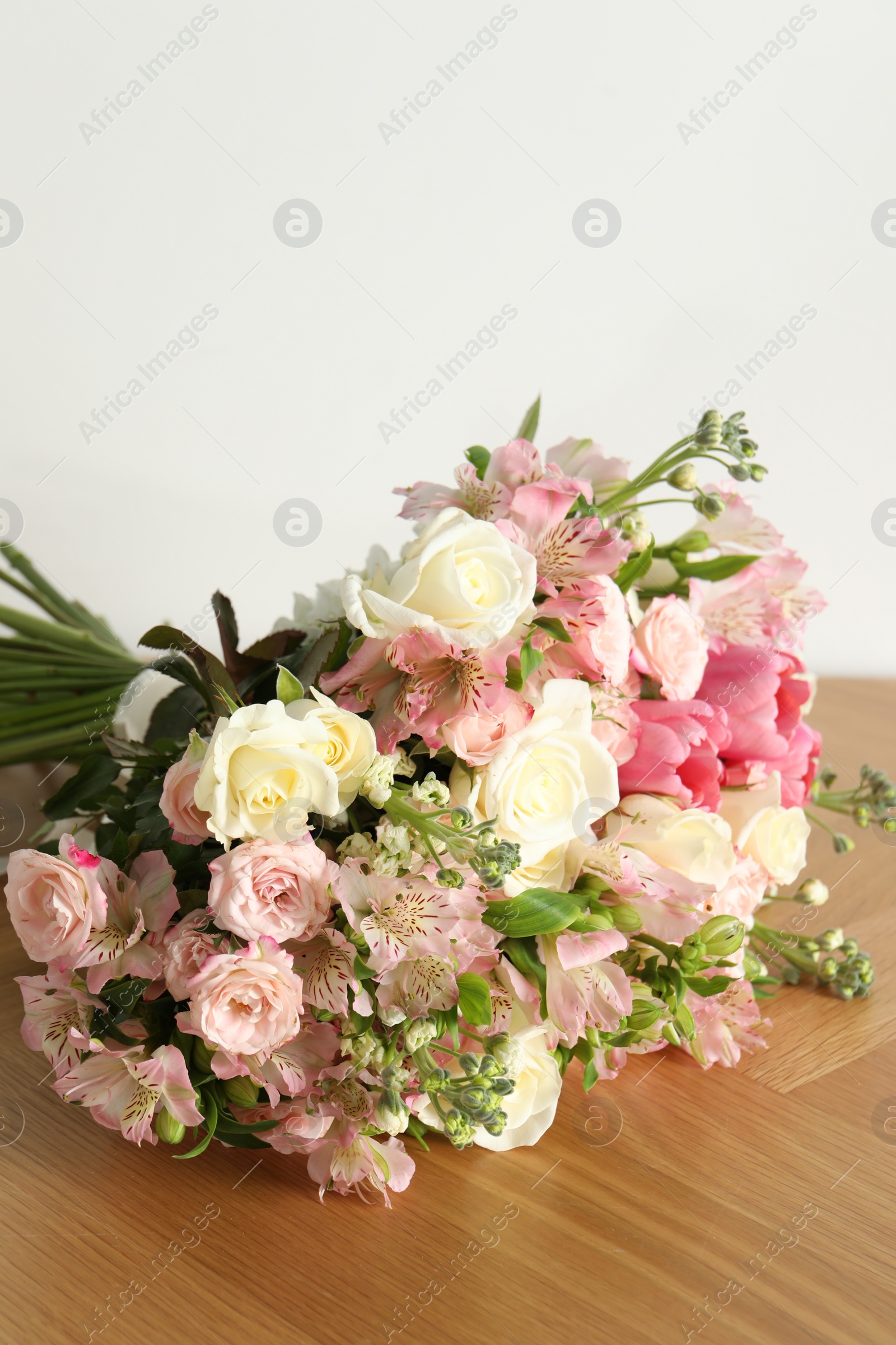 Photo of Beautiful bouquet of fresh flowers on wooden table near white wall