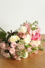 Beautiful bouquet of fresh flowers on wooden table near white wall