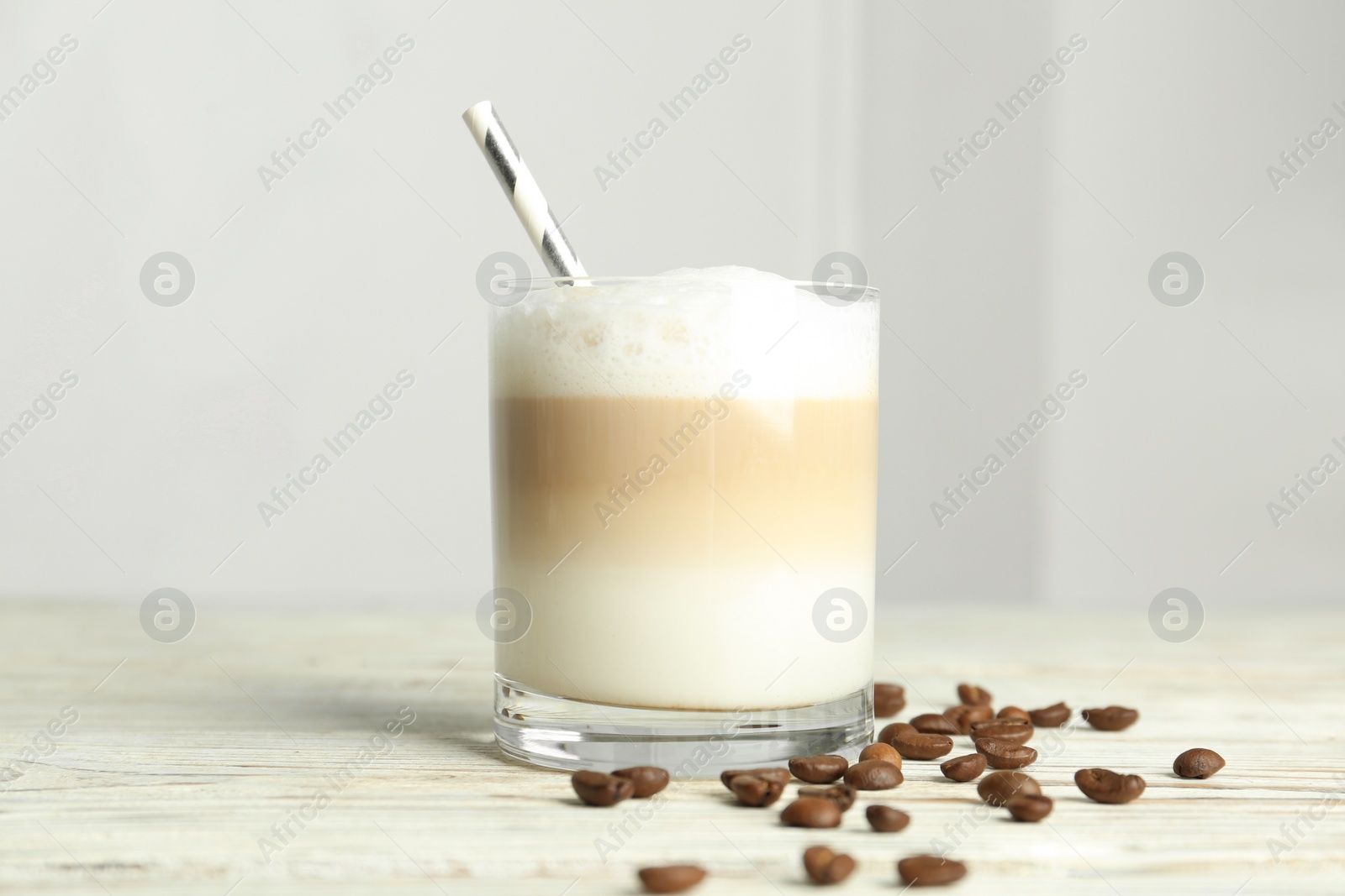 Photo of Delicious latte macchiato and coffee beans on white wooden table indoors