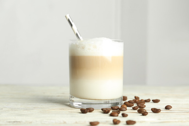 Delicious latte macchiato and coffee beans on white wooden table indoors