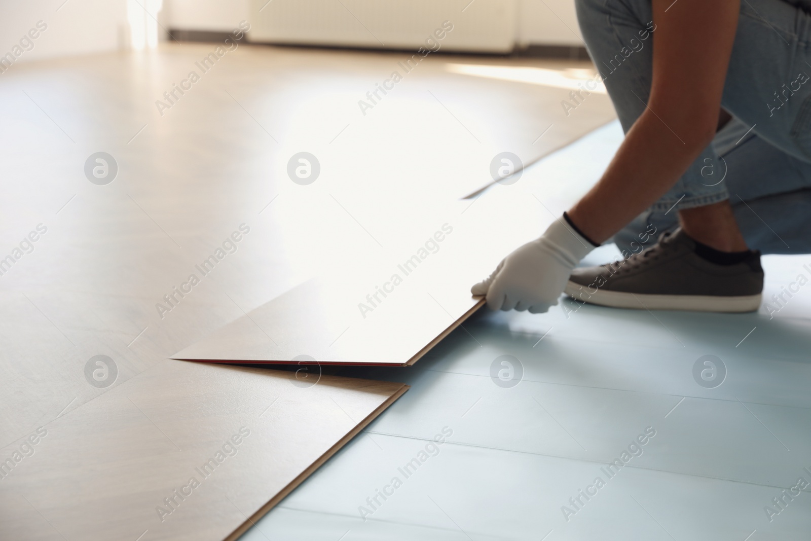 Photo of Worker installing laminated wooden floor indoors, closeup