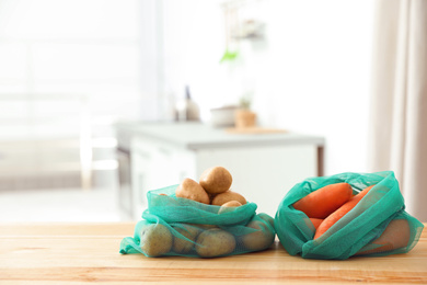 Net bags with vegetables on wooden table in kitchen