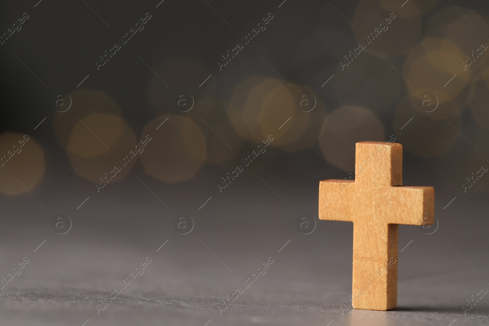 Photo of Wooden Christian cross on grey table against blurred lights, space for text