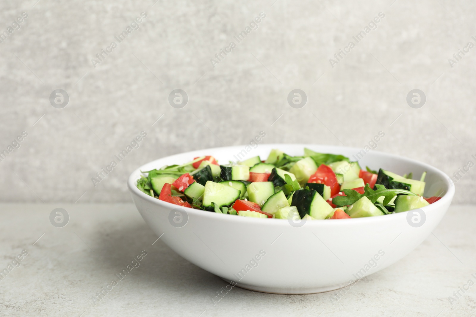 Photo of Delicious salad with cucumbers, tomatoes and sesame in bowl on light table, space for text