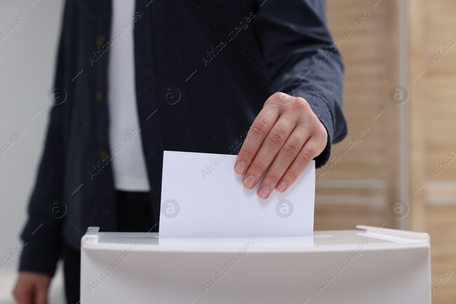 Photo of Woman putting her vote into ballot box on blurred background, closeup