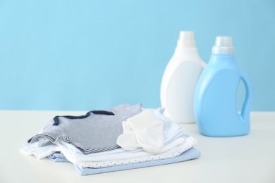 Photo of Detergents and children's clothes on white table near light blue wall. Space for text