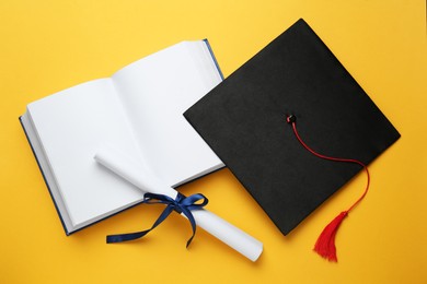 Photo of Graduation hat, book and diploma on yellow background, flat lay