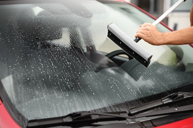 Photo of Man cleaning windshield with glass wiper, closeup. Car wash service