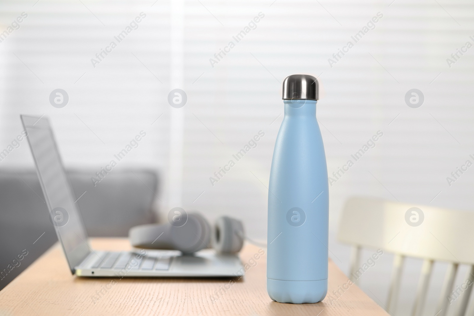 Photo of Stylish thermo bottle and laptop on wooden table at home. Space for text