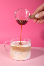 Woman making iced coffee on pink background, closeup