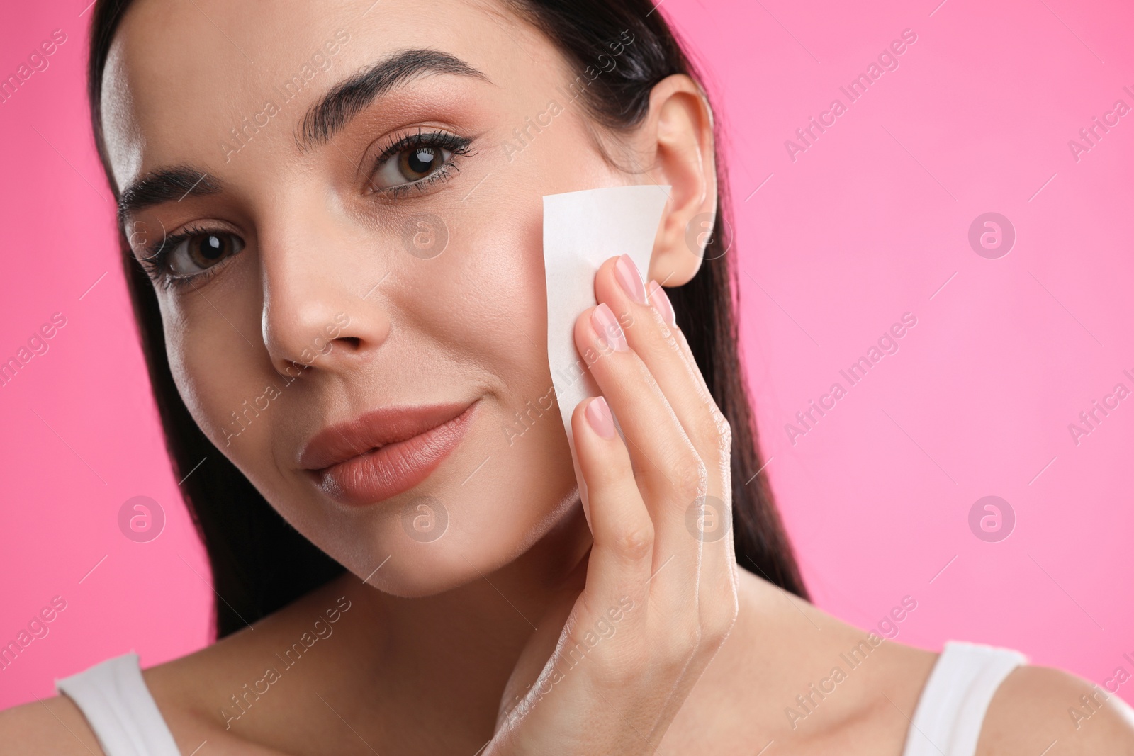 Photo of Beautiful woman using mattifying wipe on pink background, closeup