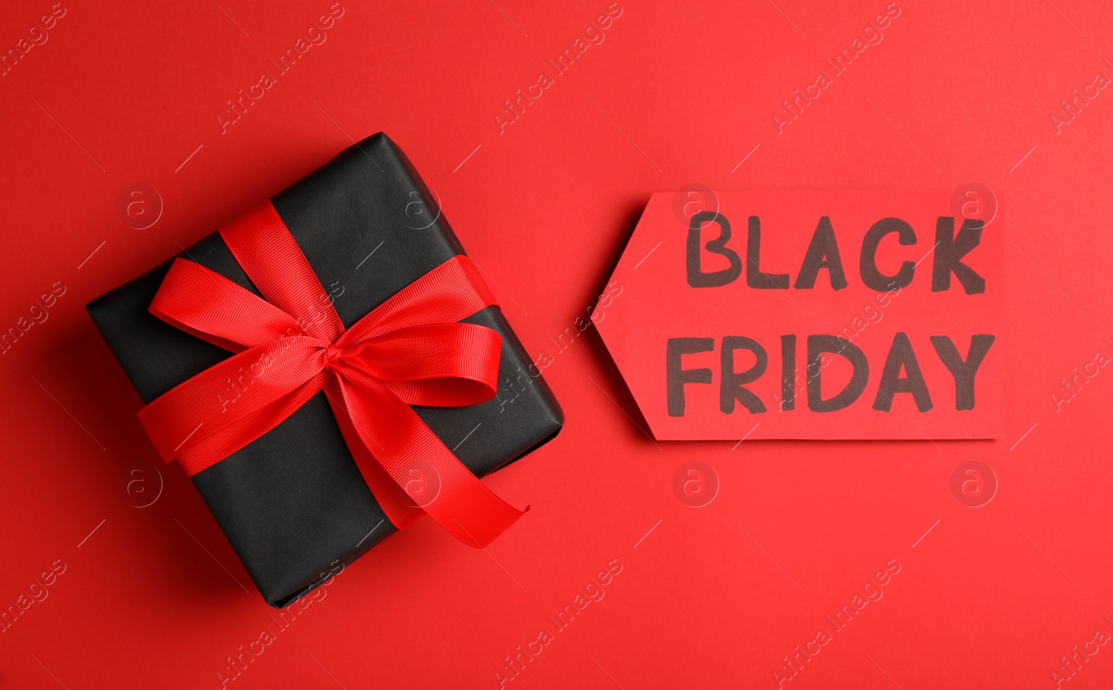 Photo of Tag with phrase Black Friday and gift box on red background, flat lay