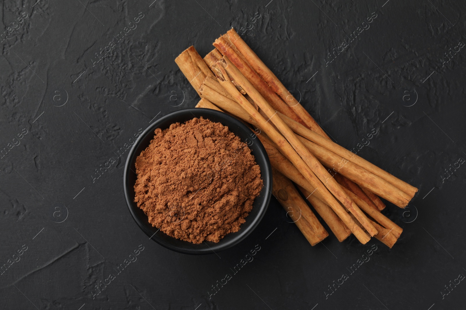 Photo of Dry aromatic cinnamon sticks and powder on black table, flat lay