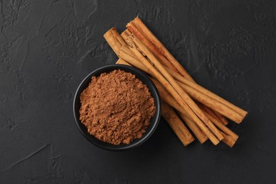 Dry aromatic cinnamon sticks and powder on black table, flat lay