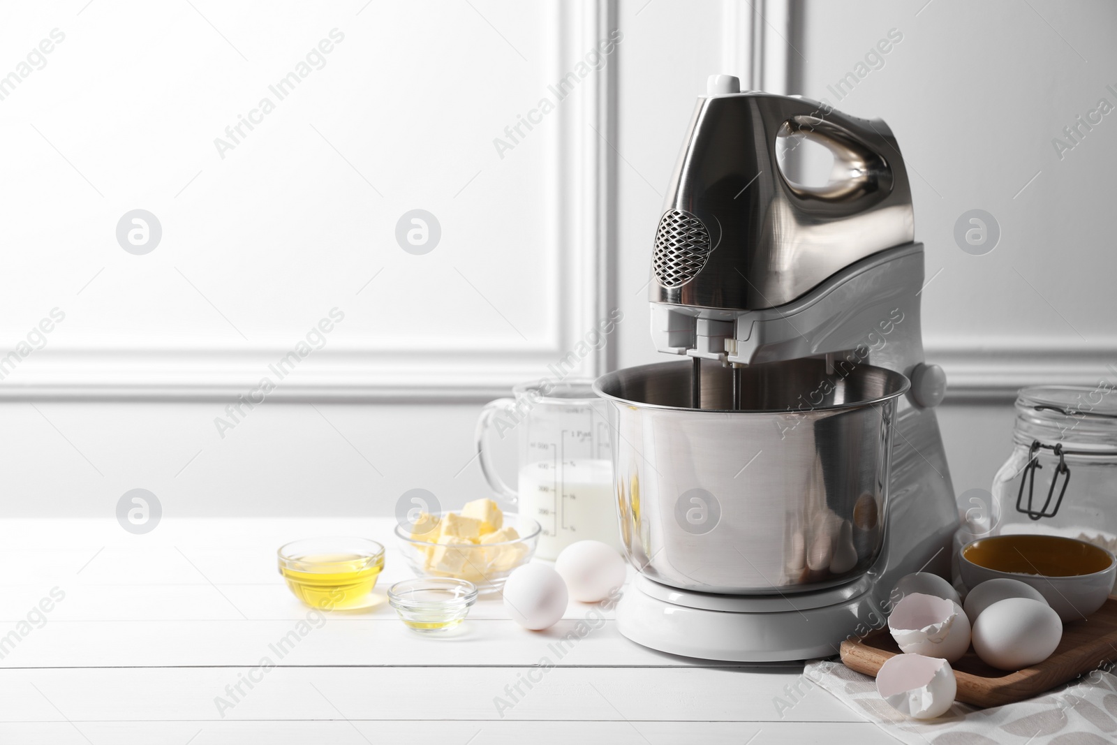 Photo of Modern stand mixer and ingredients for dough on white table indoors. Space for text