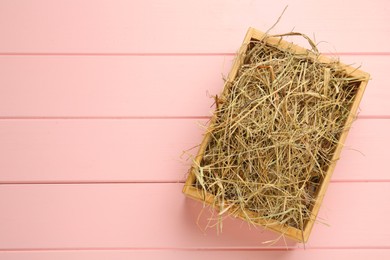 Photo of Dried hay in crate on pink wooden background, top view. Space for text