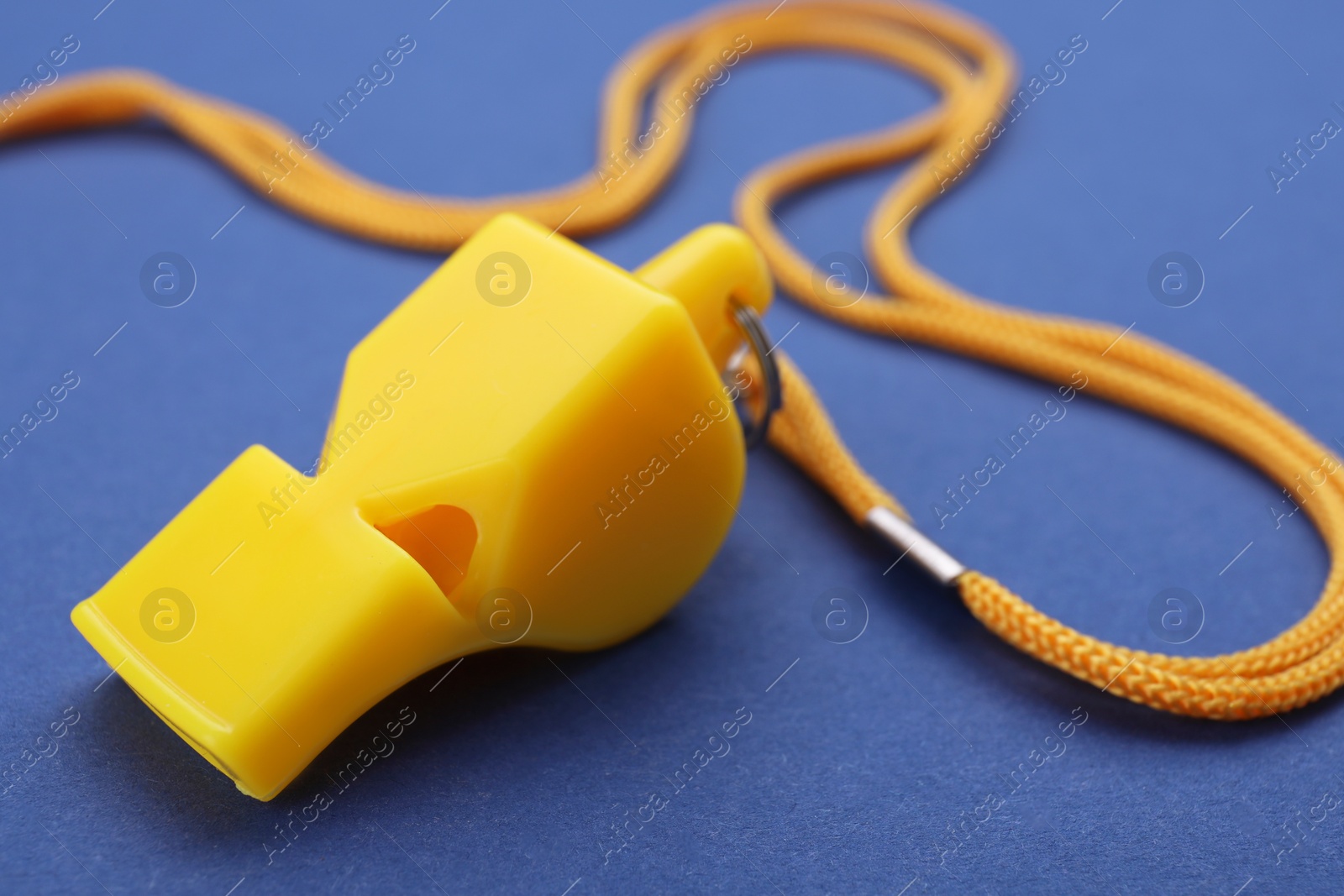 Photo of One yellow whistle with cord on blue background, closeup