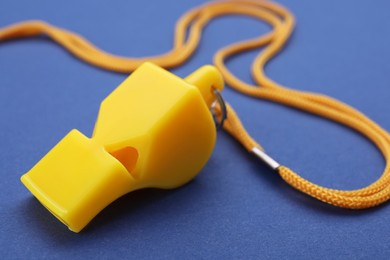 Photo of One yellow whistle with cord on blue background, closeup