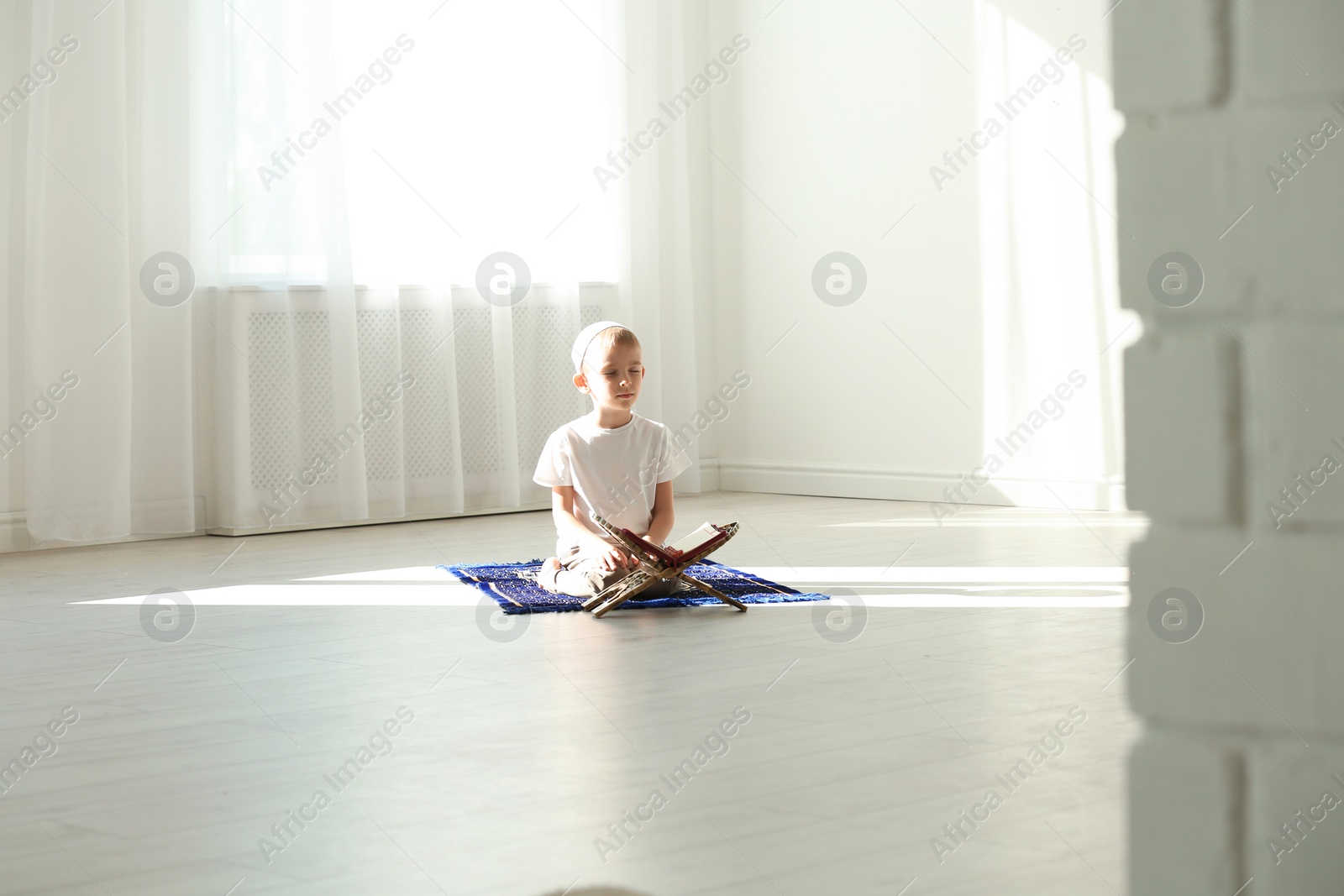 Photo of Little Muslim boy with Koran praying on rug indoors