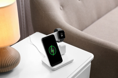 Photo of Smartphone, watch and earphones charging on wireless pad in room