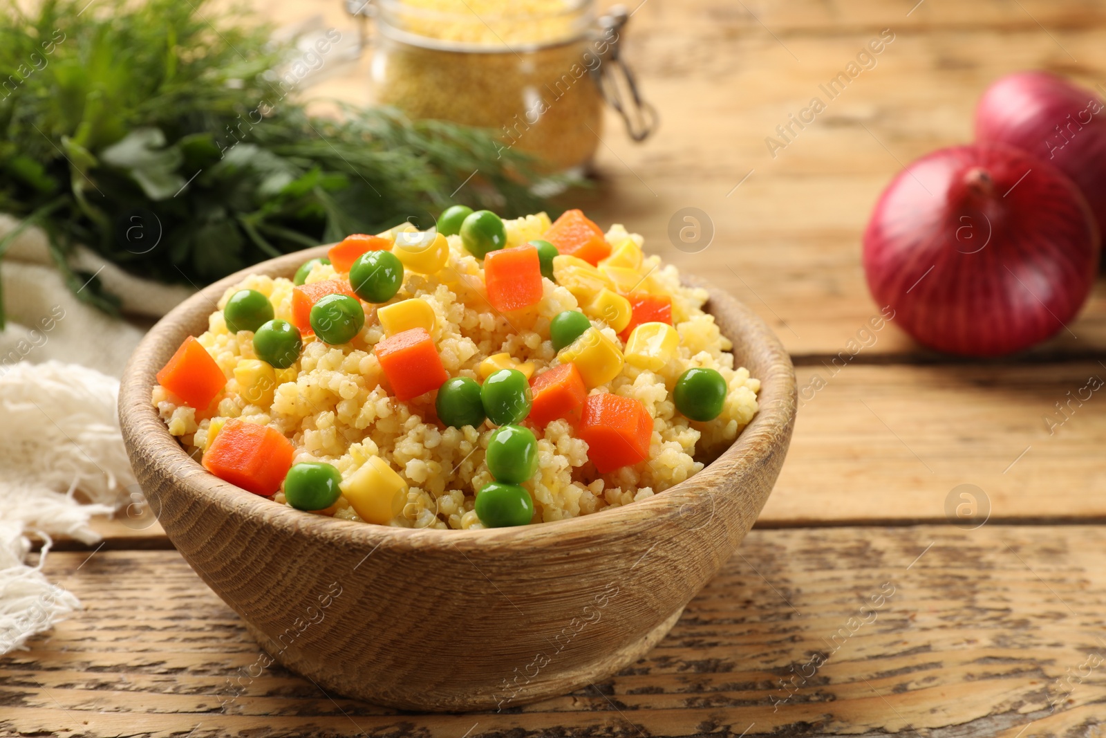 Photo of Tasty millet porridge with vegetables in bowl on wooden table, closeup