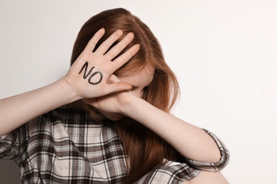 Photo of Young woman with word NO written on her palm against light background, focus on hand