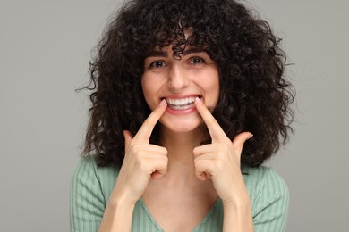 Photo of Young woman applying whitening strip on her teeth against grey background