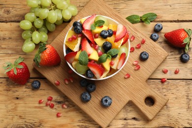 Tasty fruit salad in bowl and ingredients on wooden table, flat lay