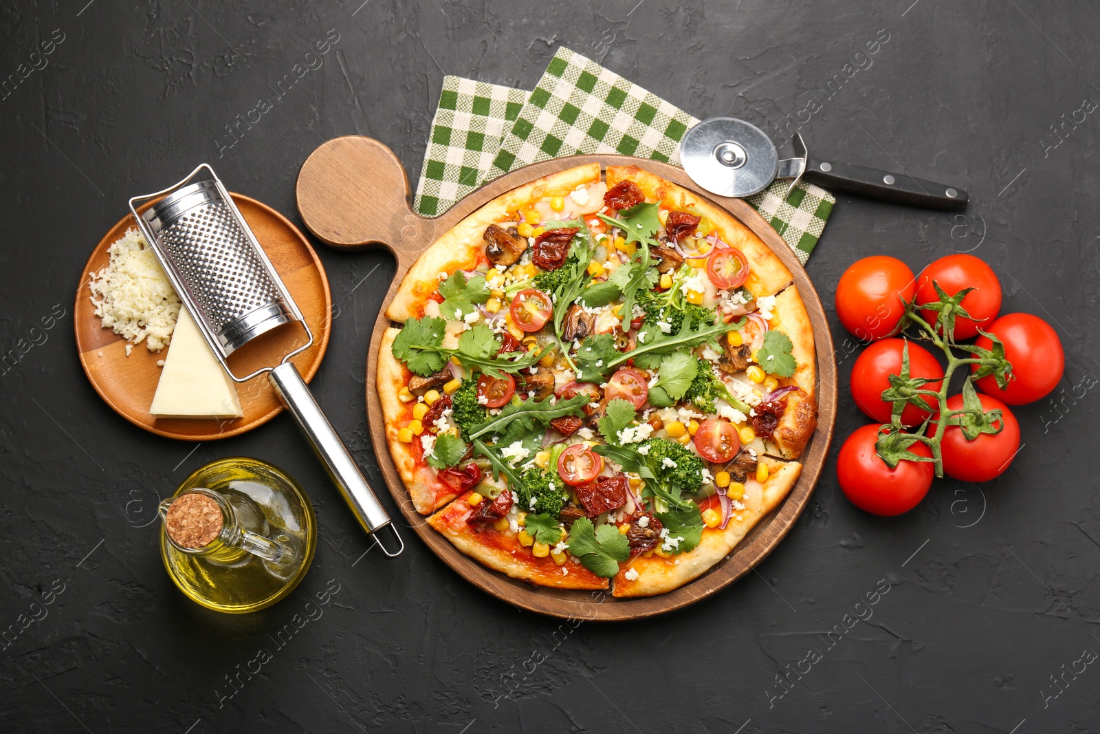 Photo of Delicious vegetarian pizza, ingredients, cutter and grater on black table, flat lay