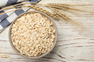 Photo of Bowl of oatmeal, napkin and spikelets on white wooden table, flat lay. Space for text