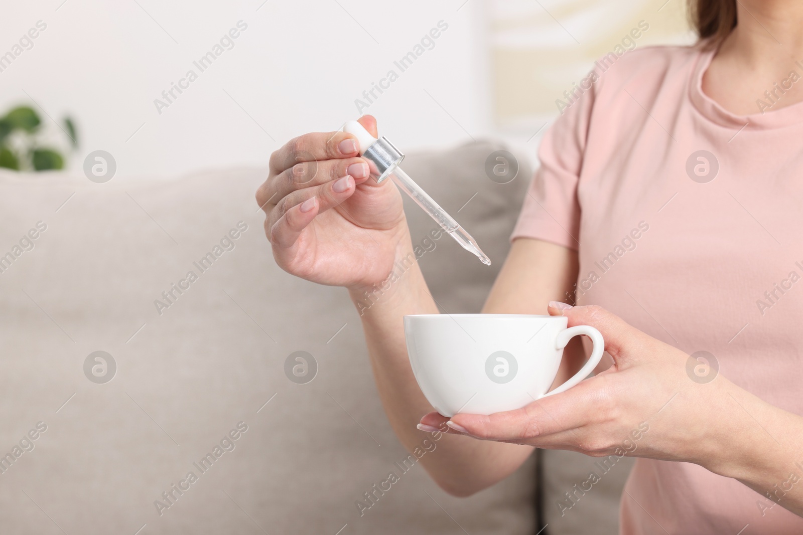 Photo of Woman dripping food supplement into cup indoors, closeup. Space for text