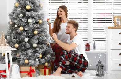 Happy young couple decorating Christmas tree at home