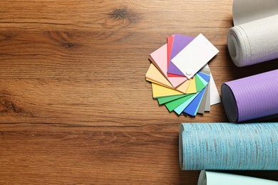 Photo of Different wallpaper rolls and color palette samples on wooden table, flat lay. Space for text