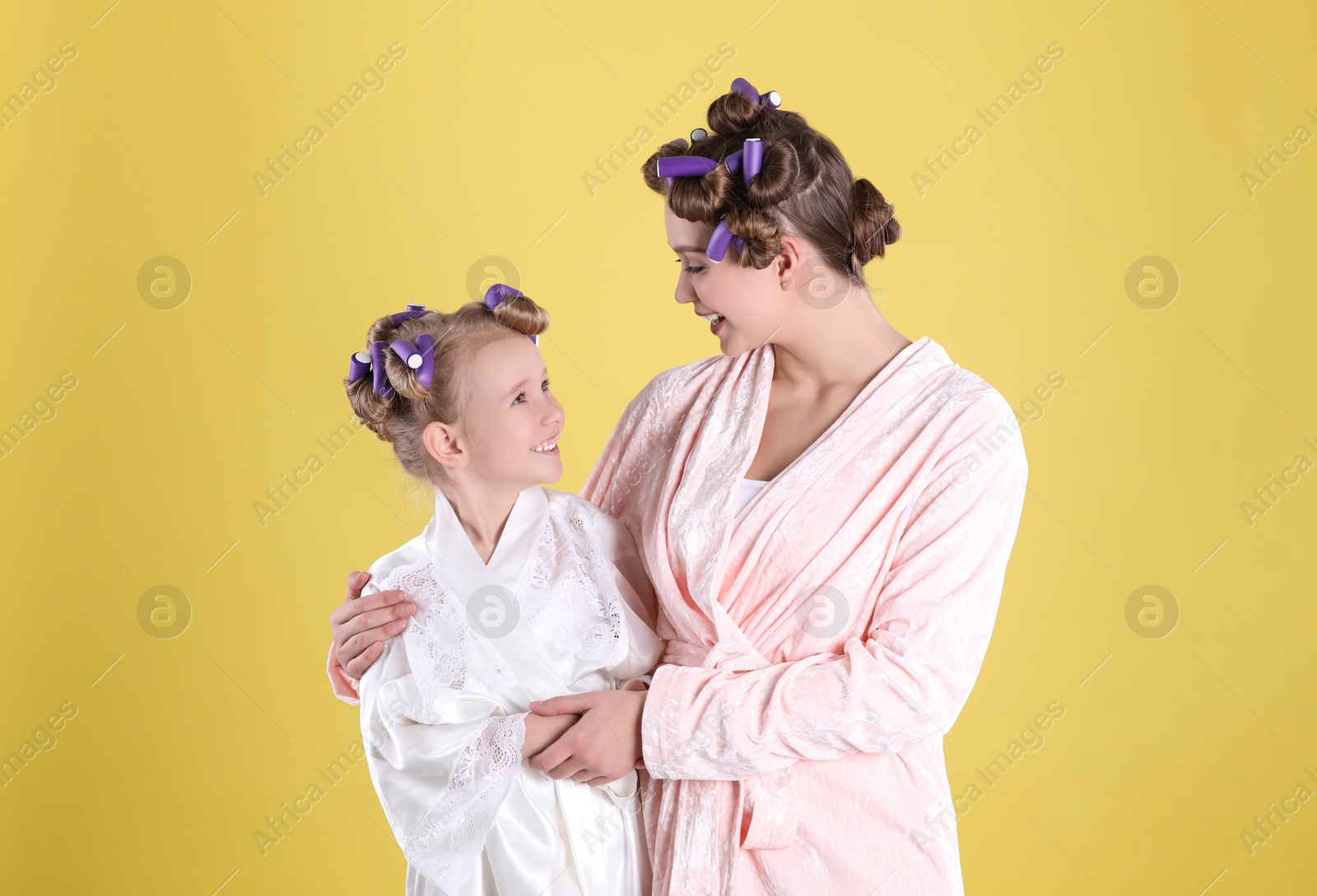 Photo of Happy mother and daughter with curlers on yellow background