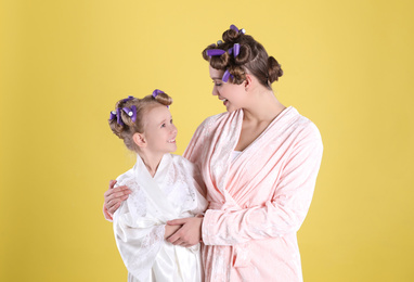 Happy mother and daughter with curlers on yellow background