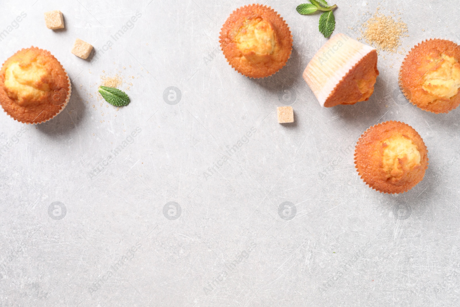 Photo of Delicious sweet muffins and brown sugar on light grey textured table, flat lay. Space for text