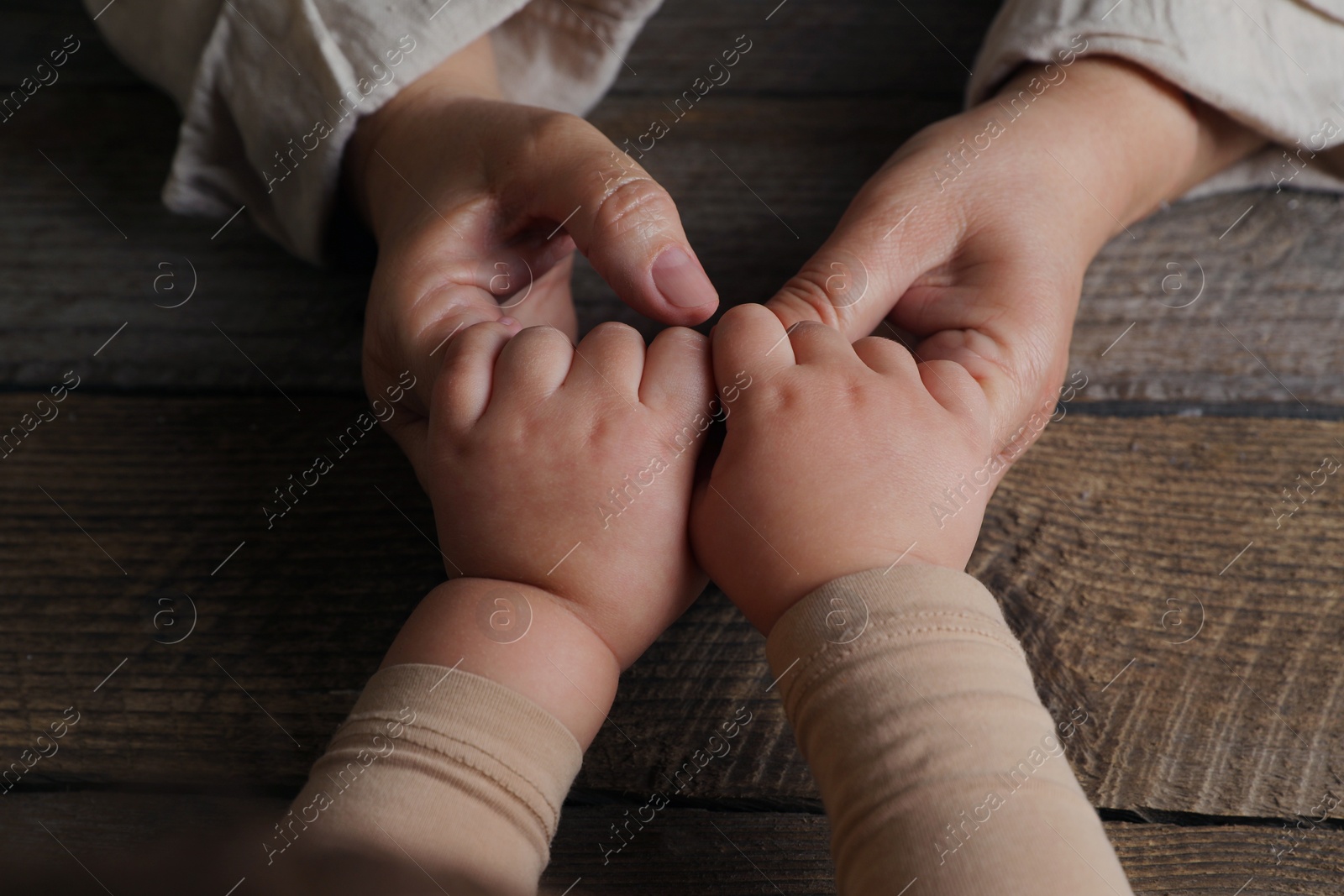 Photo of Woman holding hands with her granddaughter at wooden table, closeup