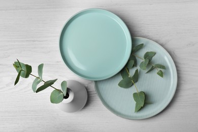 Beautiful dishware and vase with green leaves on white wooden table, flat lay