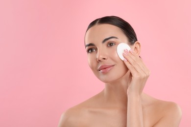 Photo of Beautiful woman removing makeup with cotton pad on pink background. Space for text