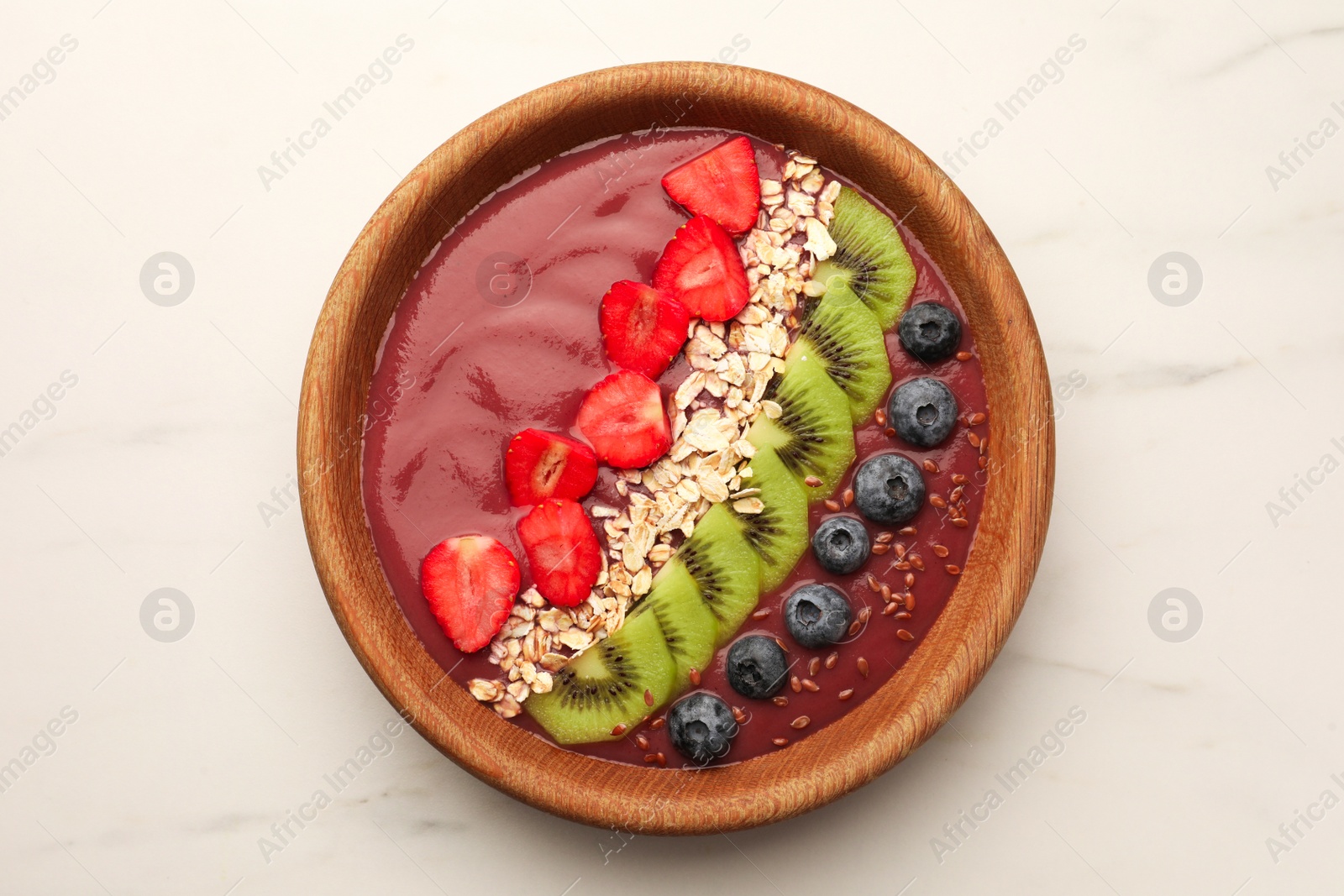 Photo of Bowl of delicious smoothie with fresh blueberries, strawberries, kiwi slices and oatmeal on white marble table, top view