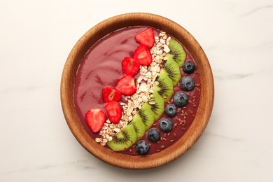Bowl of delicious smoothie with fresh blueberries, strawberries, kiwi slices and oatmeal on white marble table, top view