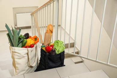 Photo of Tote bags with vegetables and other products on stairs indoors. Space for text