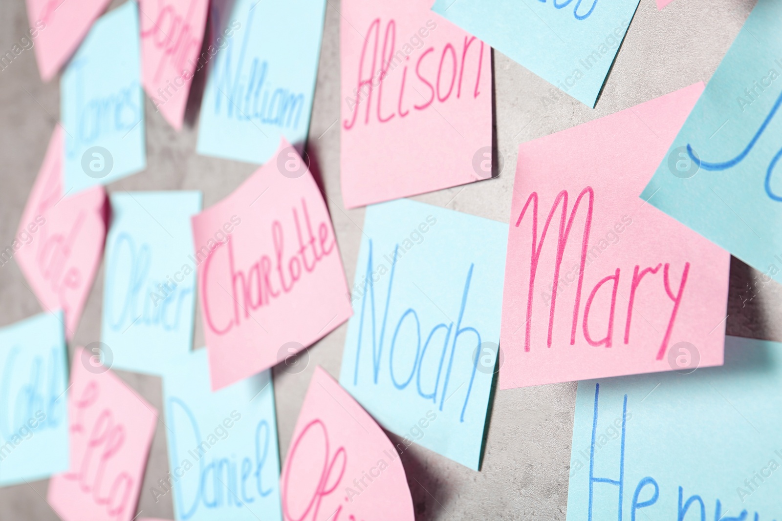 Photo of Colorful paper sheets with written different baby names on grey background, closeup