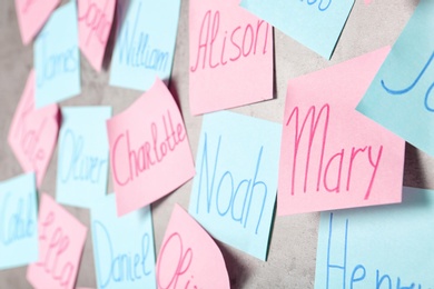 Photo of Colorful paper sheets with written different baby names on grey background, closeup