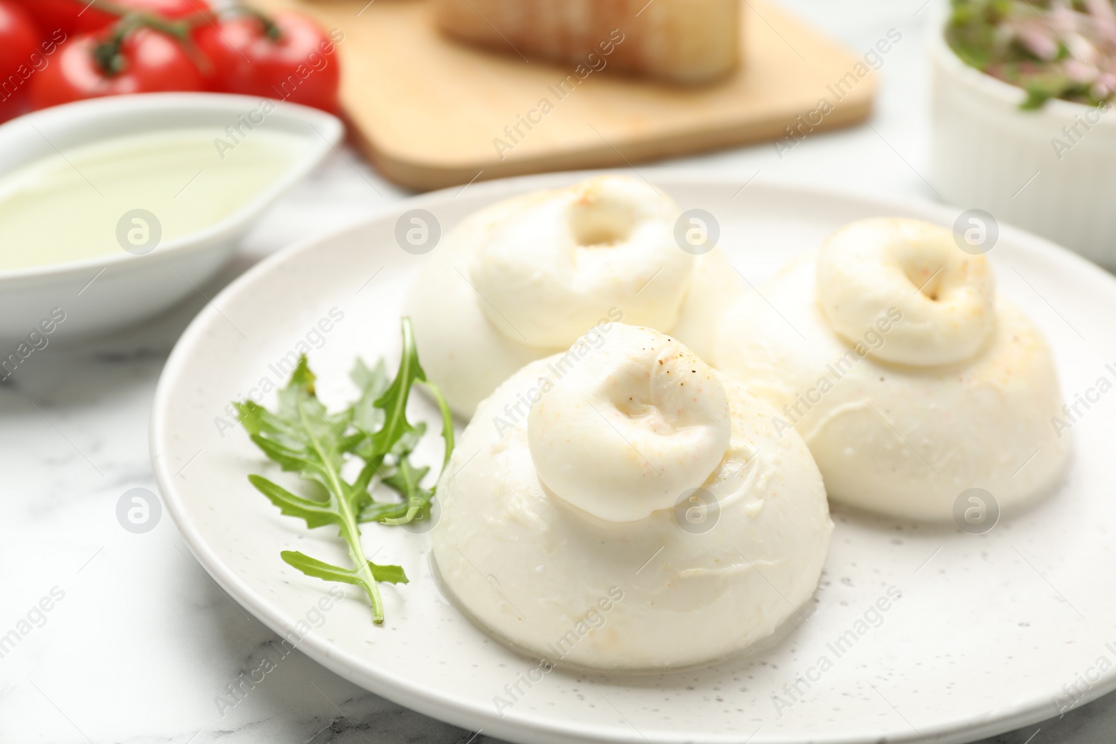 Photo of Delicious burrata cheese with arugula on white marble table, closeup