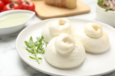 Photo of Delicious burrata cheese with arugula on white marble table, closeup