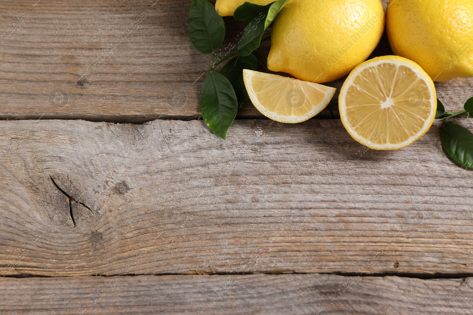 Photo of Fresh lemons and green leaves on wooden table, flat lay. Space for text