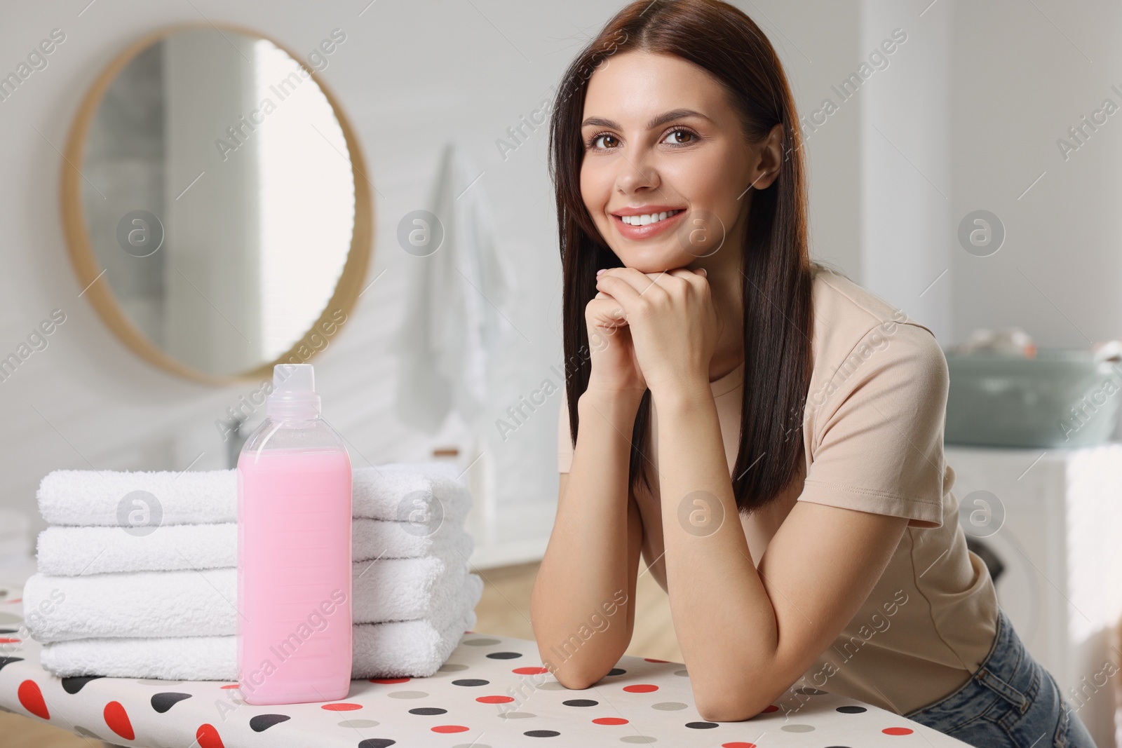 Photo of Woman near clean towels and fabric softener in bathroom