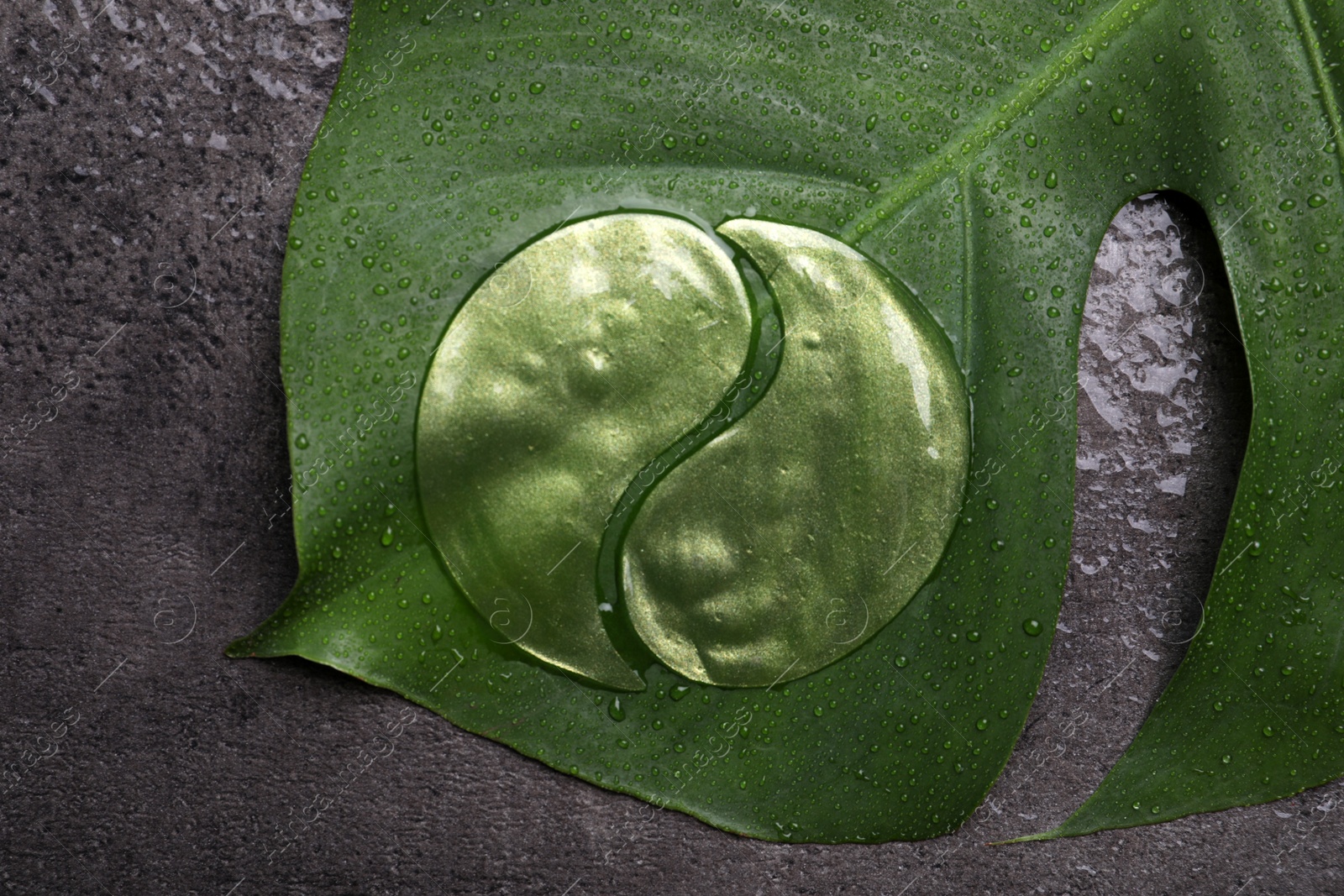 Photo of Under eye patches and tropical leaf on grey wet background, top view. Cosmetic product