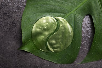 Under eye patches and tropical leaf on grey wet background, top view. Cosmetic product